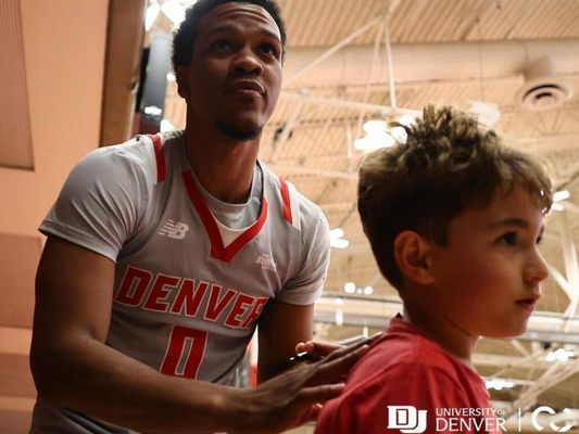 Tommy Bruner, a guard for the Denver Pioneers, looking upwards during a game. He is wearing a white and red Denver jersey with the number 0.