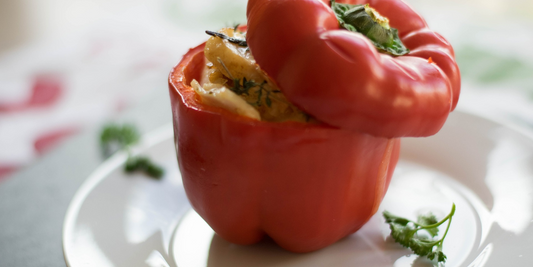 A single grilled red bell pepper with its top placed back on, served on a white plate and garnished with fresh herbs.