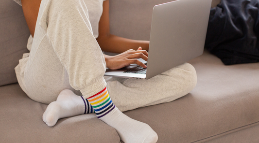 A person sitting on a couch wearing light gray sweatpants and colorful striped socks, working on a laptop.