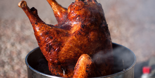 A fully cooked deep-fried turkey being lifted from a metal fryer with steam rising.