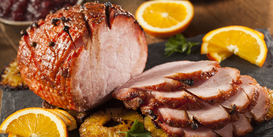 Sliced glazed ham garnished with whole cloves, orange slices, and pineapple rings on a serving platter.