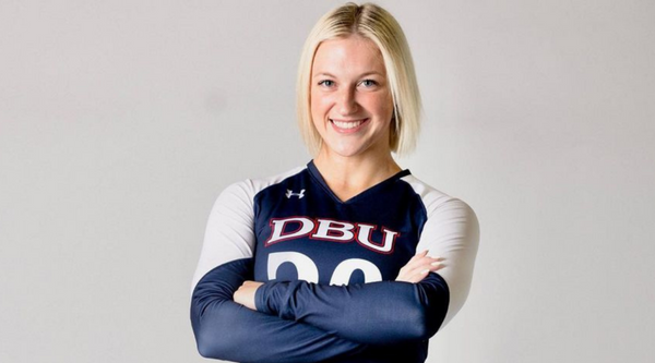 Eve Doudican, cheerleader at Dallas Baptist University, stands confidently in her DBU cheer uniform, arms crossed and smiling. The background is plain, emphasizing her strength and presence.