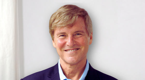 Close-up portrait of Leigh Steinberg, smiling in a navy blue suit against a light background.