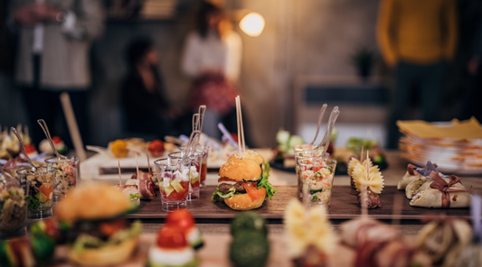 A buffet table with a variety of appetizers, including mini burgers, wraps, skewers, and small salad cups, set in a warm and festive gathering space.