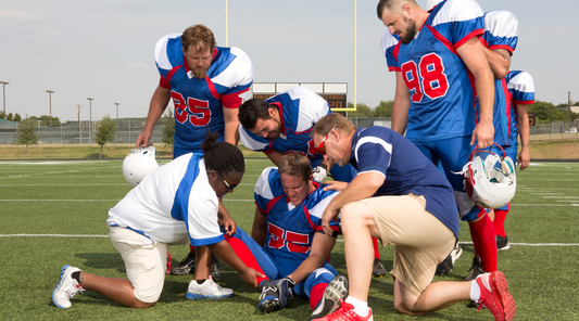 A football player sitting on the field surrounded by teammates and medical staff, receiving assistance after an injury.