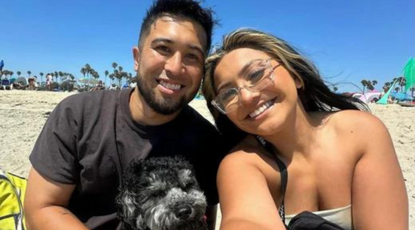 Jackie Ramirez and Nico Blitz, co-hosts of the Mexipino Podcast, smile for a selfie at the beach with their black and white dog.
