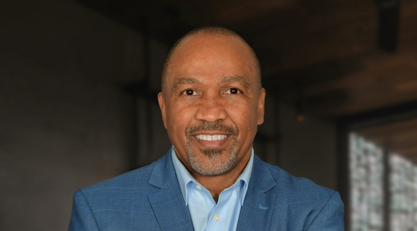 Mark Jackson poses confidently in a blue blazer and light blue shirt, smiling with arms crossed.