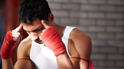 A young boxer with red hand wraps concentrates deeply, pressing his fingers to his temples, symbolizing mental preparation and focus.