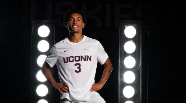 Mikah Thomas, a soccer player in a white jersey, signs an autograph for a young fan wearing an orange Thunderbolt Jets shirt at an evening event.