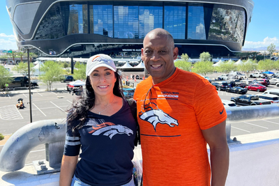 Mike Evans, founder of Fan Day Nation, and his wife wearing Denver Broncos gear outside a stadium, smiling and standing together.