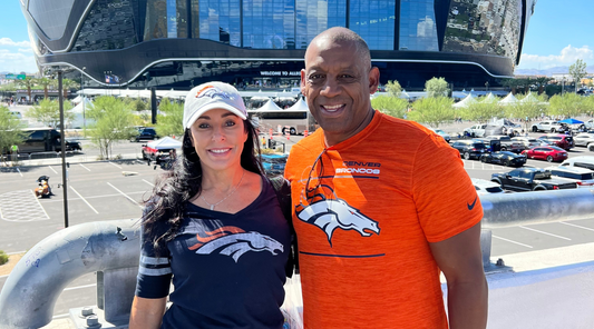 Mike Evans, founder of Fan Day Nation, and his wife wearing Denver Broncos gear outside a stadium, smiling and standing together.