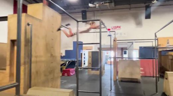 Nadia Barghelame, a young parkour athlete, is captured mid-air as she performs a dynamic parkour jump between structures in an indoor training gym.