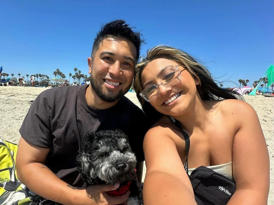 Jackie Ramirez and Nico Blitz, co-hosts of the Mexipino Podcast, smile for a selfie at the beach with their black and white dog.