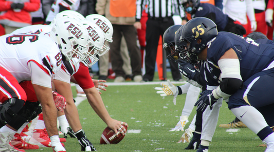 Football teams lined up at the scrimmage line during a rivalry game, showcasing intense focus and determination on the field.