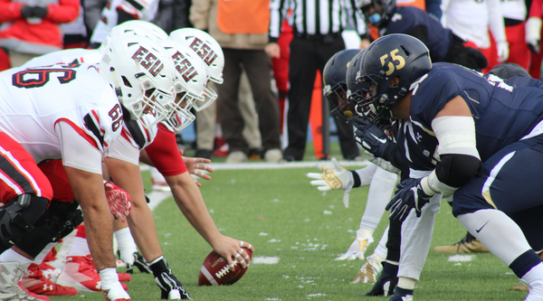 Football teams lined up at the scrimmage line during a rivalry game, showcasing intense focus and determination on the field.