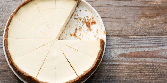 A whole plain cheesecake with slices cut out on a wooden table.