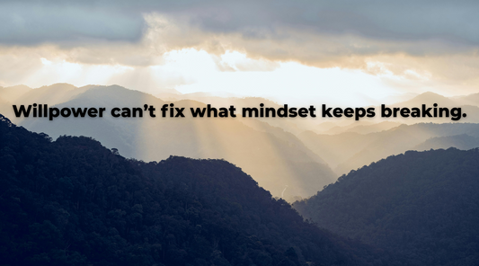 Sunlight breaking through clouds over a mountain range with the text “Willpower can’t fix what mindset keeps breaking.”