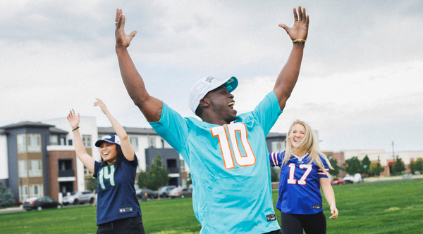 Group of sports fans outdoors, wearing jerseys and celebrating with raised arms.